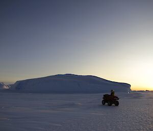 A large ice berg stuck in the fast ice in the distance with a quad bike and rider in the foreground