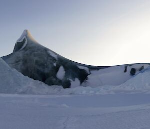 A beautiful dark green Jade ice berg partly covered in snow standing out in the full sun