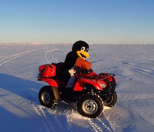 An expeditioner in a penguin suit sitting on a quad bike out on the frozen sea ice with snow covered islands in the back ground