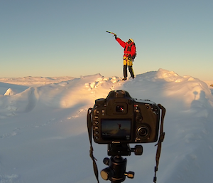 Picture of camera filming expeditioner standing on a snow bank in full search and rescue gear looking out over horizon