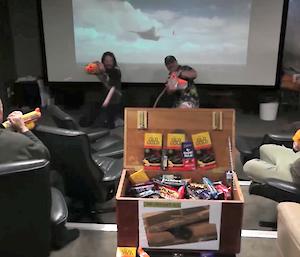 Expeditions in the cinema surrounding a large wooden chocolate box firing nerf guns at each other