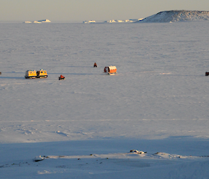 An alternative picture of expeditioners on quad bikes and Hägglunds approaching the Rimmet Van on the frozen sea ice with Gardener Island and icebergs in the background