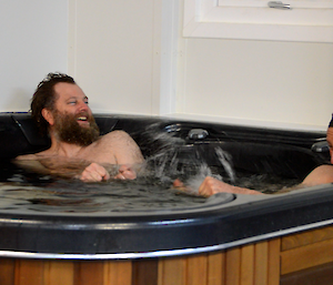 Picture of two expeditioners in the spa bath squirting water with their hands at each other. One is smiling, the other squinting after getting water in his eye