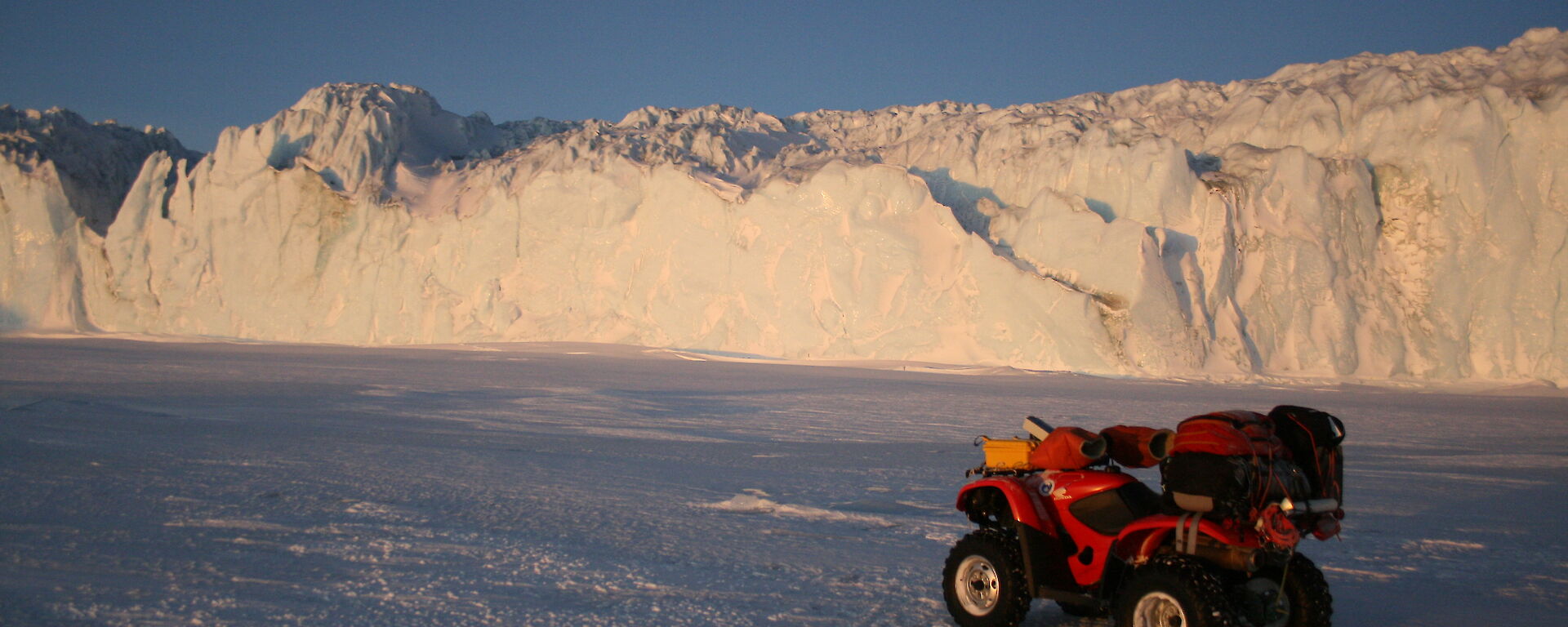 Red quad bike parked on the sea ice with the enormous glacier wall in the background