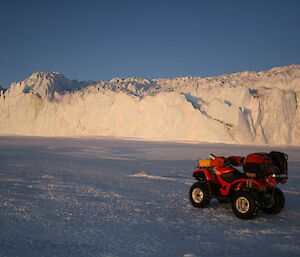 Red quad bike parked on the sea ice with the enormous glacier wall in the background