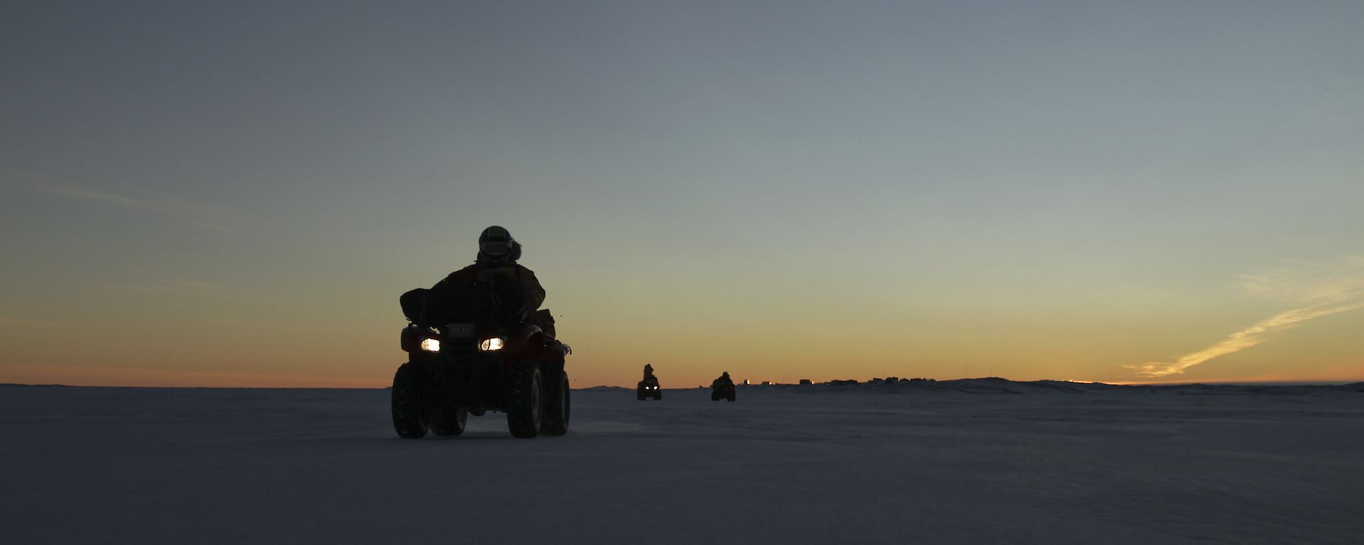 Expeditioners on the sea ice on quads with sunrise and Davis Station in the background