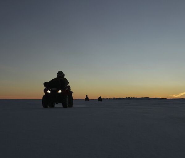 Expeditioners on the sea ice on quads with sunrise and Davis Station in the background