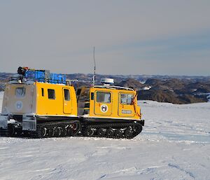 Yellow Hägglunds driving on the plateau with Vestfold hills behind