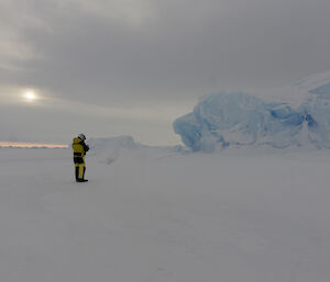 Rich standing on the sea ice taking a photo of an iceberg