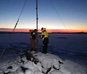 Two expeditioners working on a antenna in the field with a lovely sunset as the backdrop