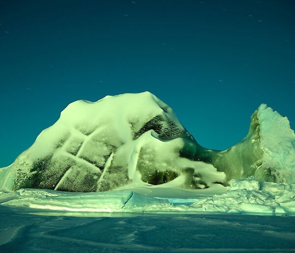 A lightly snow covered jade ice berg under the moon light on a very clear night