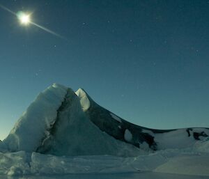 The moon high in the sky above a jade ice berg