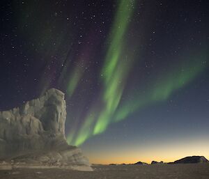 A green aurora drifting across the night sky with an ice berg in the foreground