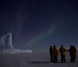 Four expeditioners stand on the sea ice with a dim aurora in the night sky