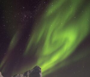 A green aurora drifting across the night sky with an ice berg in the foreground