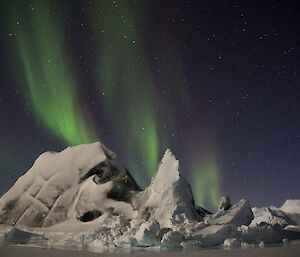 A green aurora drifting across the night sky with a jade ice berg in the foreground