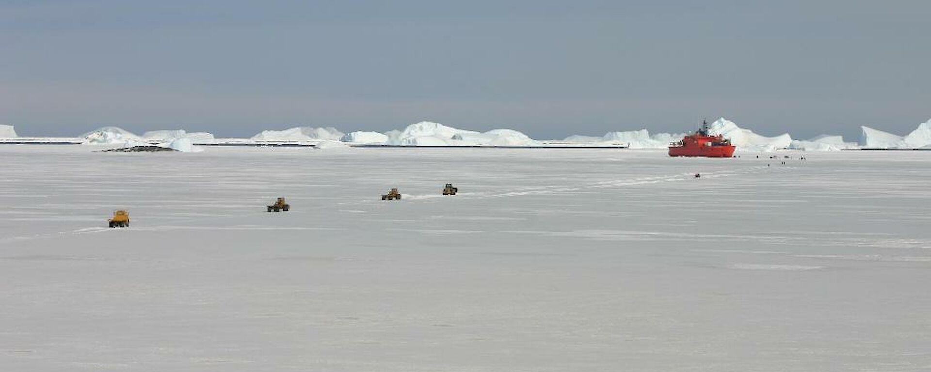 The Aurora Australis parked in the sea ice with several heavy vehicles driving out over the sea ice to start a resupply