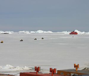 The Aurora Australis parked in the sea ice with several heavy vehicles driving out over the sea ice to start a resupply