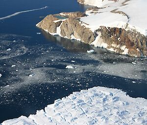 Photo taken from a helicopter of a rocky outcrop with a small lake on the edge of the polar ice cap