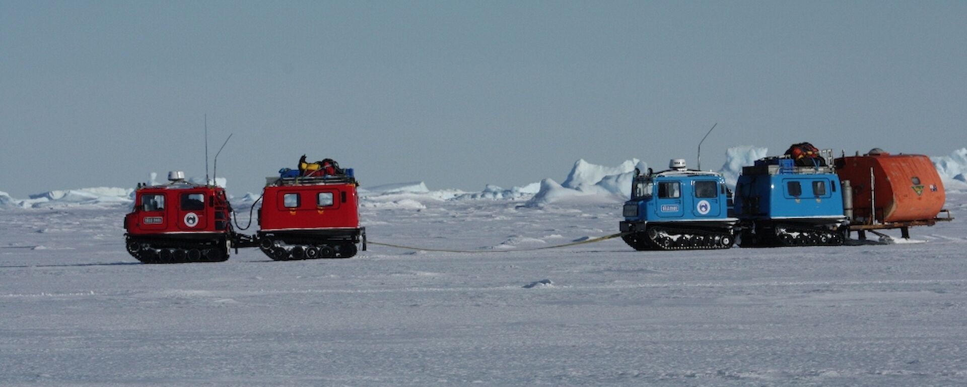 The red Hägglunds vehicle towing the blue Hagg and van on the sea ice