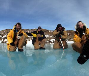 Four expeditioners sitting on a frozen fresh water melt lake for a group photo