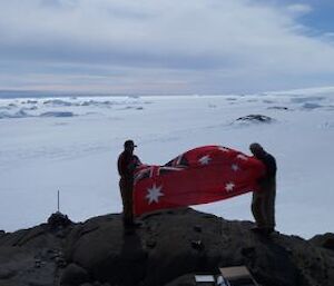 Expeditioners holiding a flag over a cairn