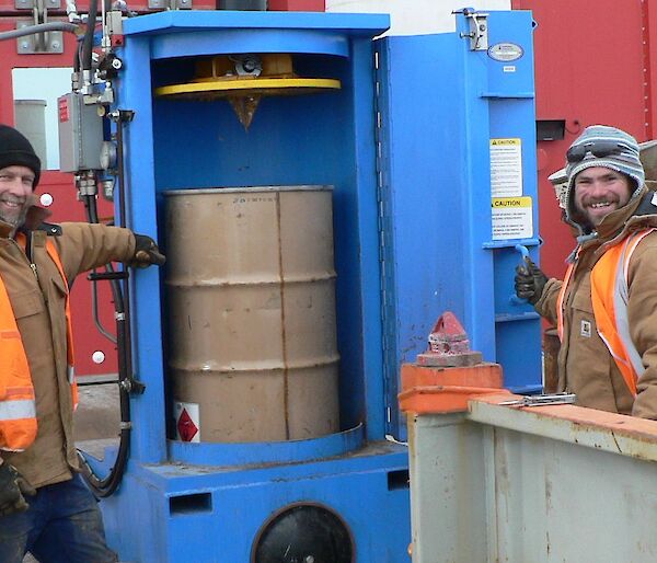 Two expeditioners standing next to a drum crusher