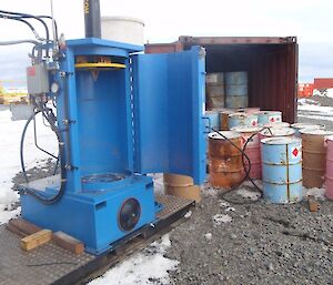 The empty drum crusher next to a container of empty fuel drums.