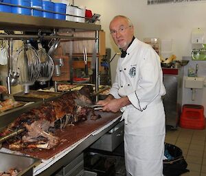 A chef cutting up a whole cooked lamb in the kitchen
