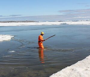 An expeditioner in a dry suit in the water breaking up the ice