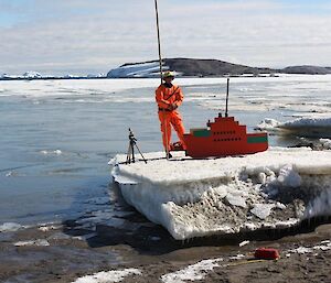 An expeditioner in a dry suit standing on a block of ice