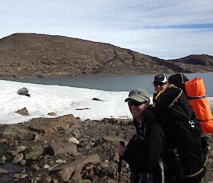 Two expeditioners face the camera while a weddell seal languishes on the ice