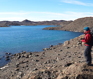 An expeditioner standing next to a lake, taking in the scenery