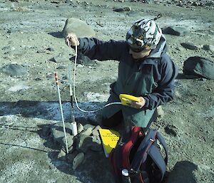 An expeditioner taking a measurement down a bore hole