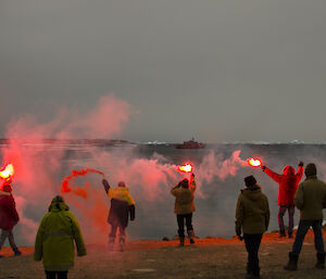 expeditioners with lit flares looking out to the ship