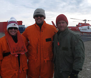 3 expeditioners posing for the camera, helicopter in background