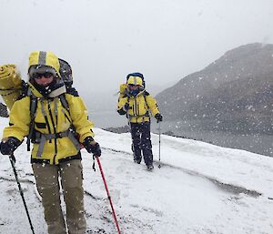 Two expeditioners in yellow windproof clothing walking into the wind and snow