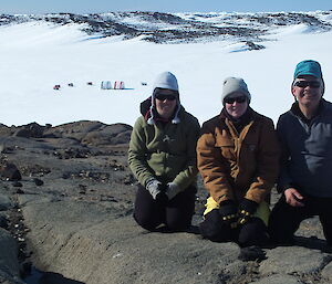Close up of 3 expeditioners with science camp site in the background