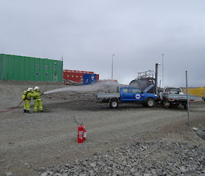 two expeditioners with a large fire fighting hose aimed at a vehicle