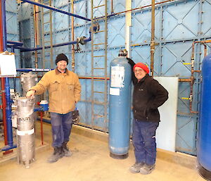 two men standing in front of large blue tank