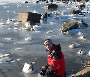 expeditioner kneeling at the frozen lakes edge