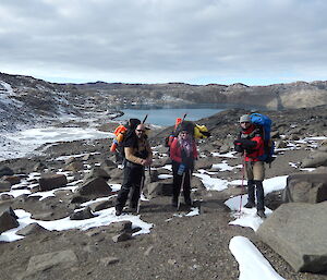 3 expeditioners with packs on with a lake in the background