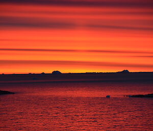 bright red and orange sunset over the water and islands