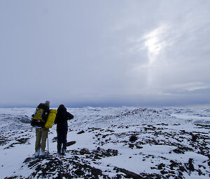 Two expeditioners standing on a high point looking out over an icy valley