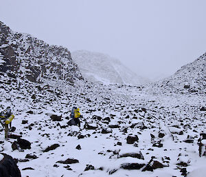 two expeditioners walking over snow and boulders