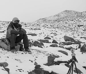 Black and white photo of expeditioner sitting on his pack with his GoPro brand camera