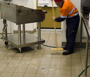 tradesman on a broom sweeping water down a drain