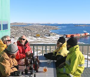 Expeditioners sitting around a table on the verandah, bay in the background