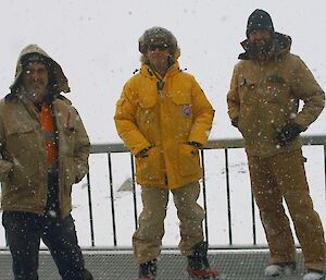 three expeditioners standing outside whilst snow is falling around them