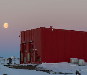 full moon and sunset over a large red building